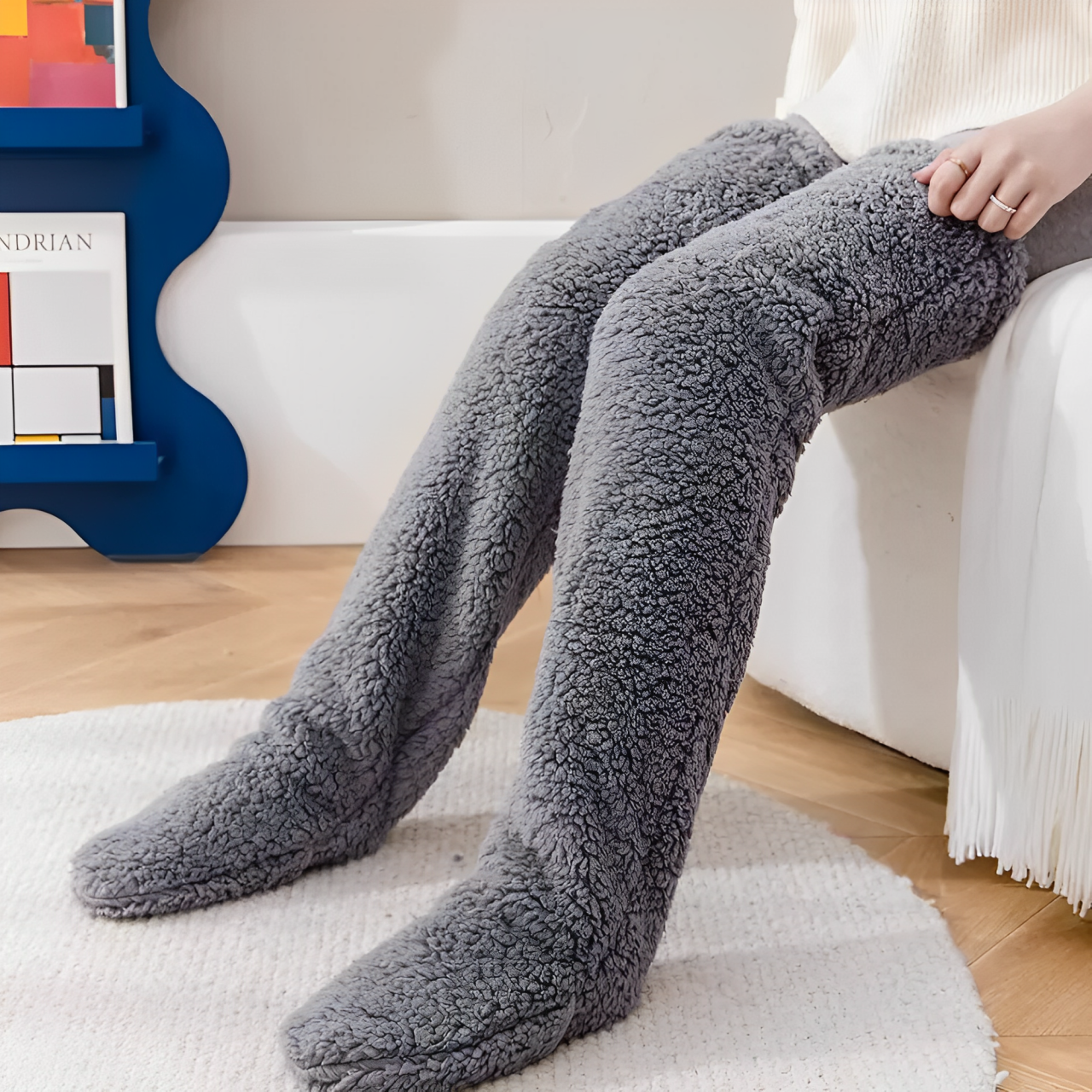 A woman sitting down and wearing dark gray plush knee high socks.