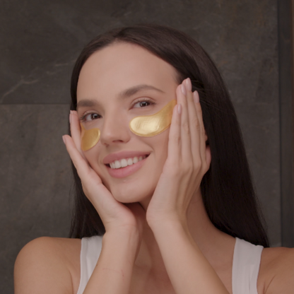 A woman wearing 24k gold eye mask under her eyes and holding her face.