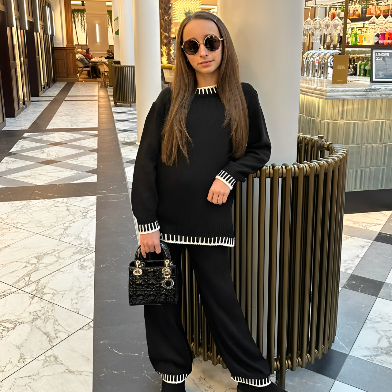 A woman standing in the mall and wearing black knitted sweater and pants set.